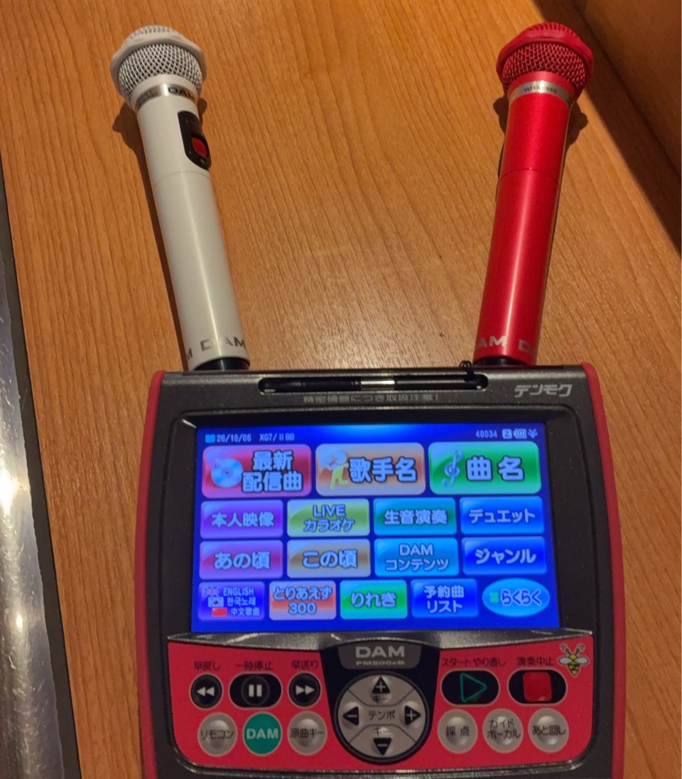 木のテーブルに置かれた赤と白のカラオケマイクと、選曲用のリモコン